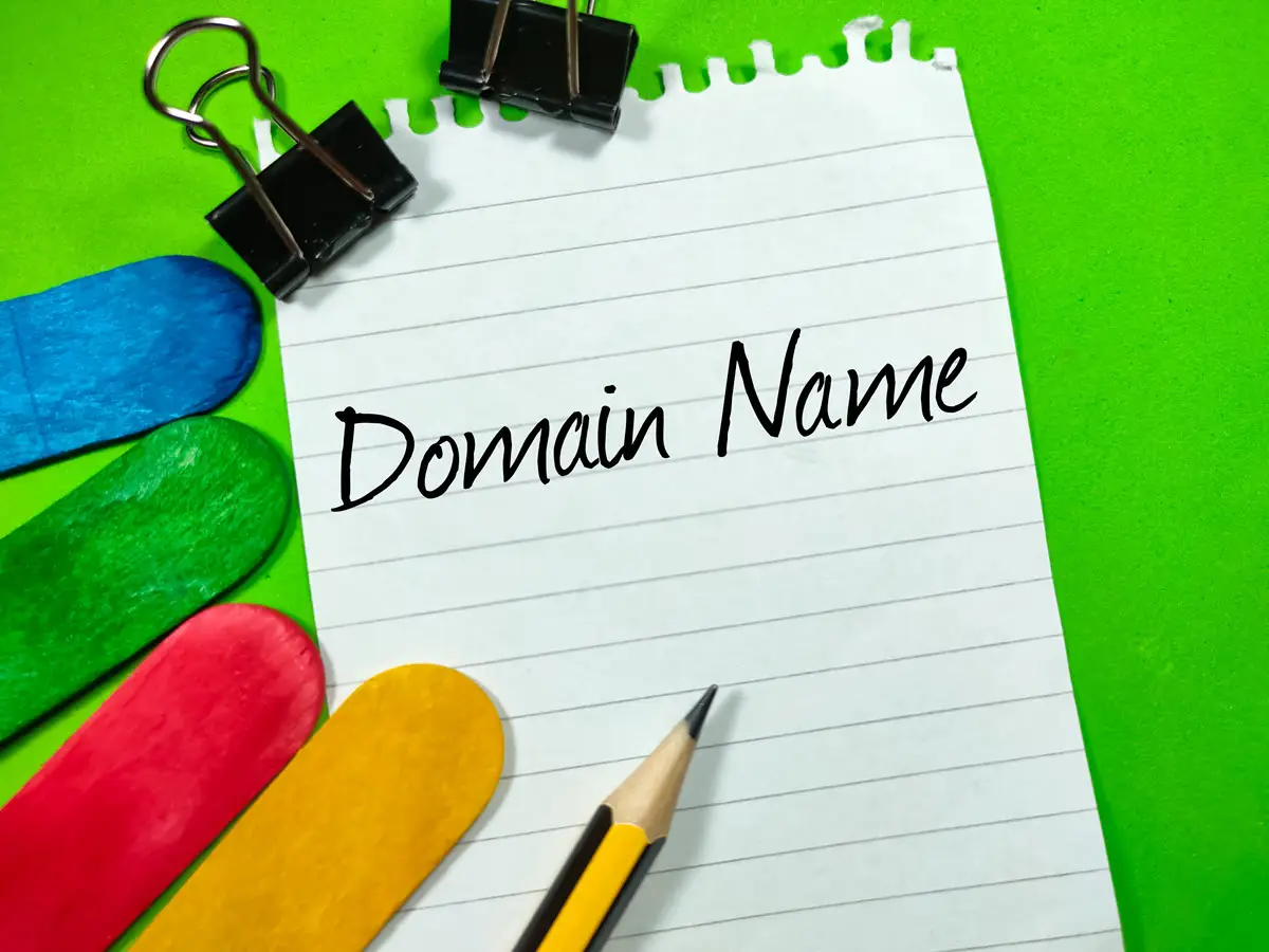 Piece of paper sitting on a green background with two paper clips, four sticks and a pencile. The words 'Domain Name' are typed on the page.